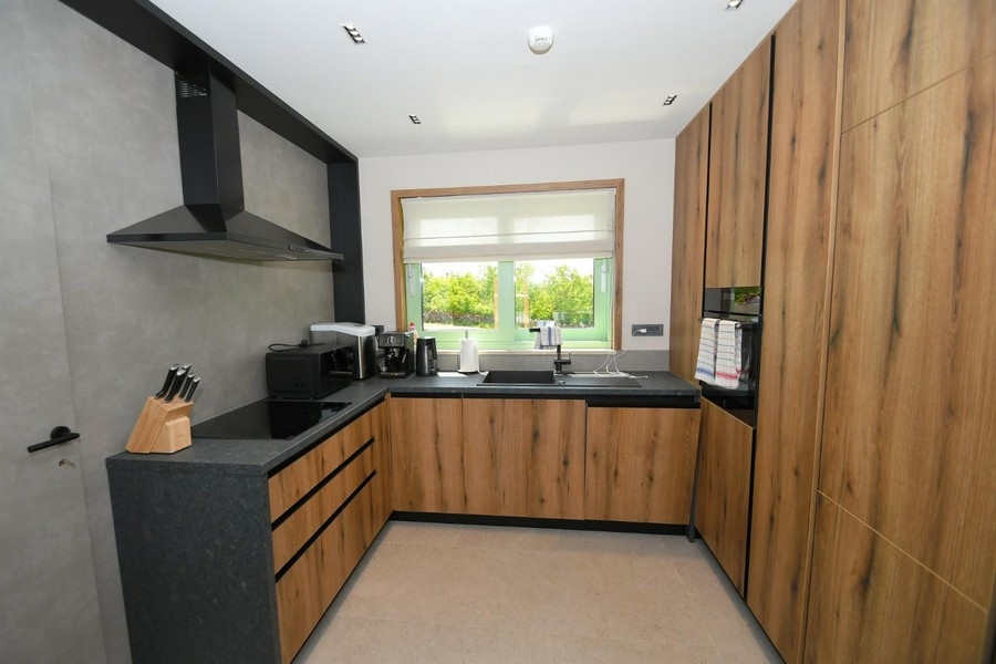 Moderní kuchyně s dřevěným obložením, černými pracovními deskami a kuchyňskými spotřebiči