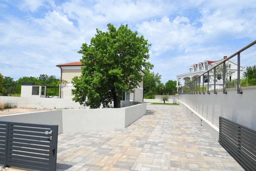Velká dlážděná venkovní plocha se stromem a moderním oplocením