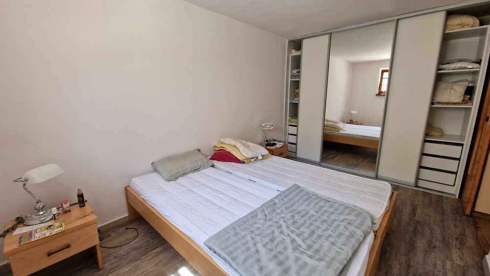 Ložnice s manželskou postelí, velkou skříní a minimalistickým nábytkem.