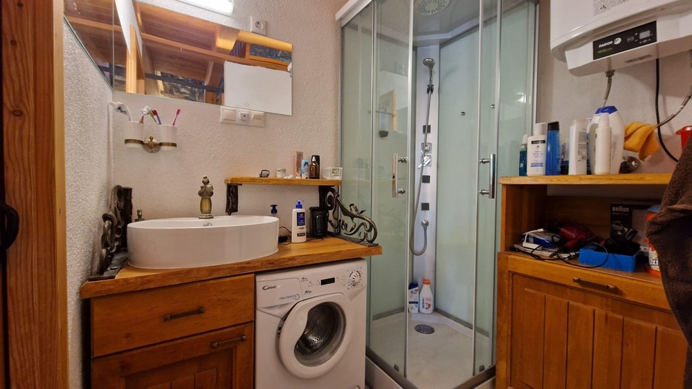 Koupelna se sprchovým koutem, pračkou a dřevěnými policemi.