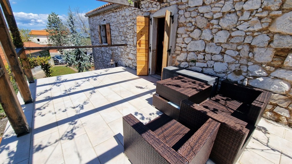 Sluneční terasa s posezením před rustikálním kamenným domem.
