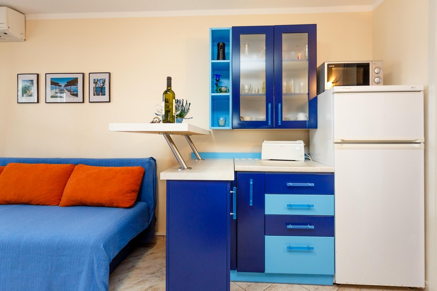 Kuchyň s modrými skříňkami, bílou lednicí a malým kuchyňským náčiním