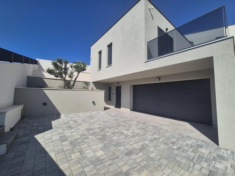 Pohled z terasy na moře a okolní domy, moderní budova se sloupy a skleněným zábradlím