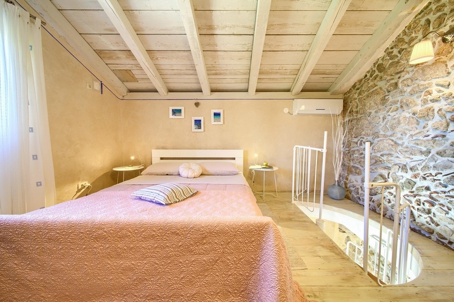Ložnice s dřevěným trámovým stropem a rustikálním nábytkem, přístupná po točitém schodišti.
