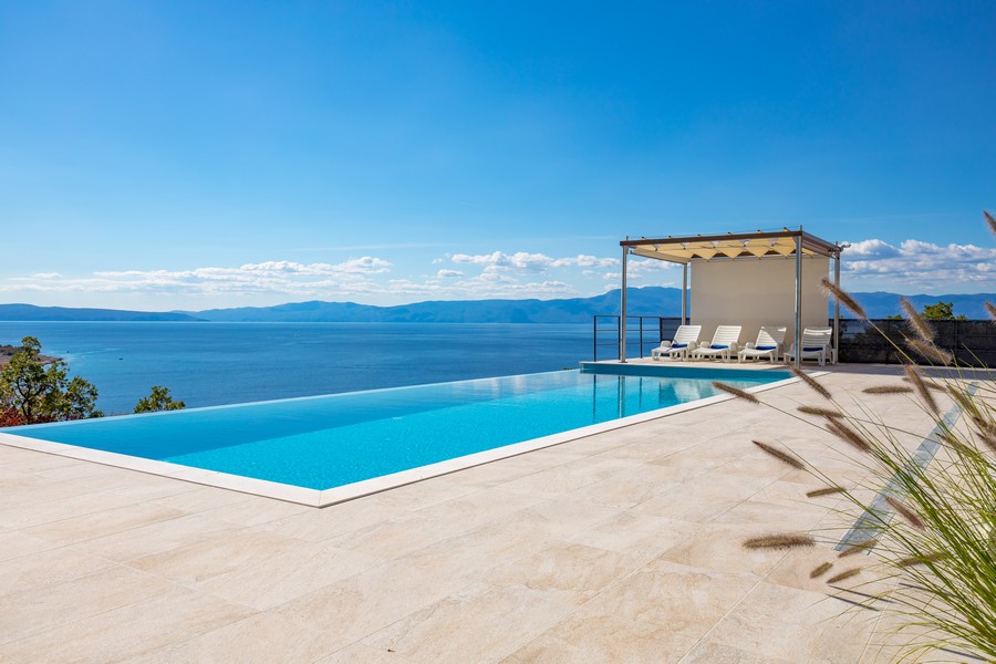 Nekonečný bazén s lehátky, přímý výhled na moře a modrá obloha.