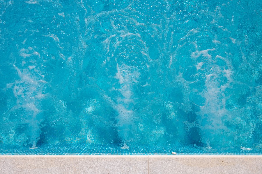 Detail bazénu, bublající vody a jasně modrých dlaždic.