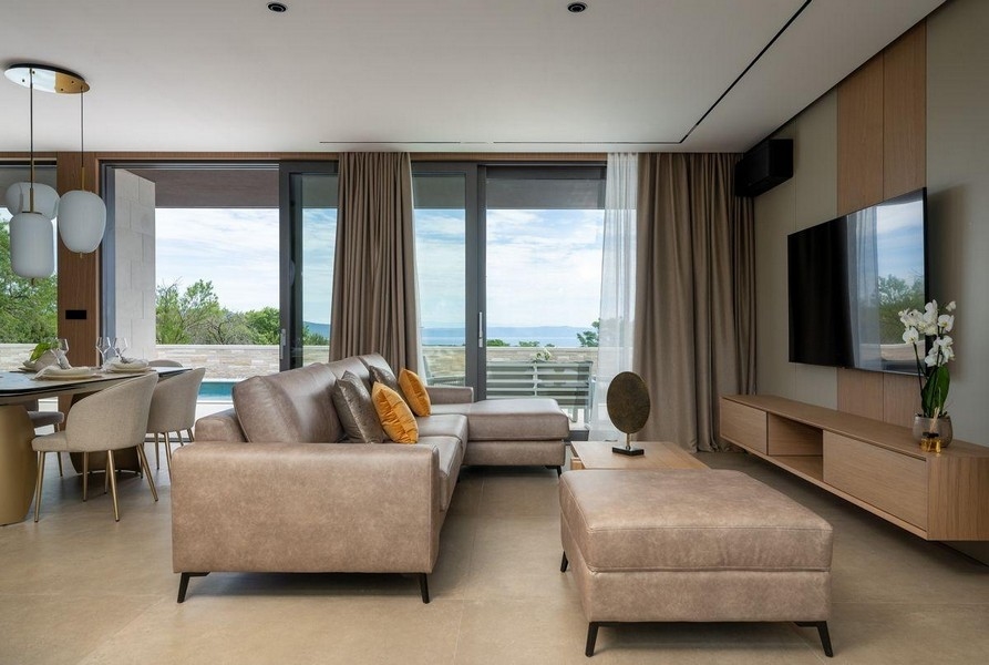 Obývací pokoj s velkými prosklenými okny a výhledem na bazén