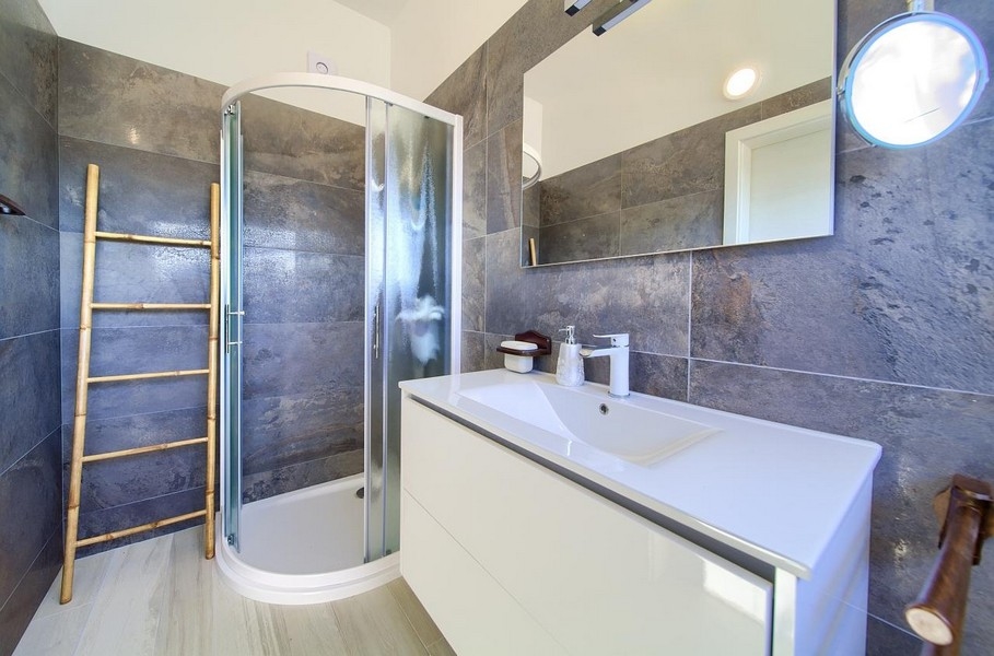 Moderní koupelna se sprchovým koutem, šedými obklady a bílým umyvadlem