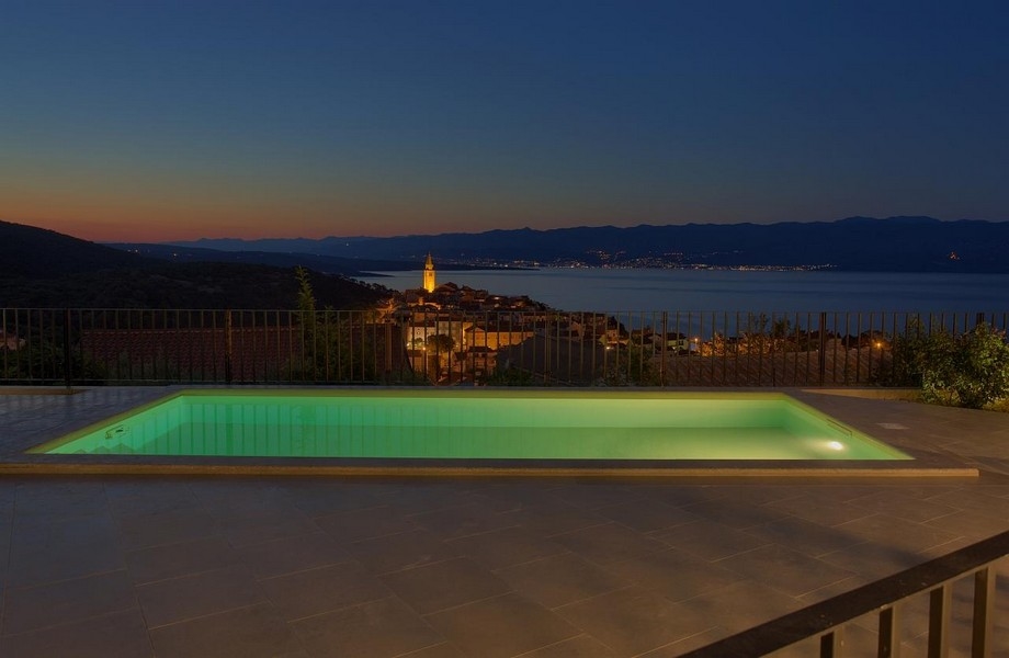Osvětlený bazén v noci a výhled na Vrbnik v Chorvatsku.