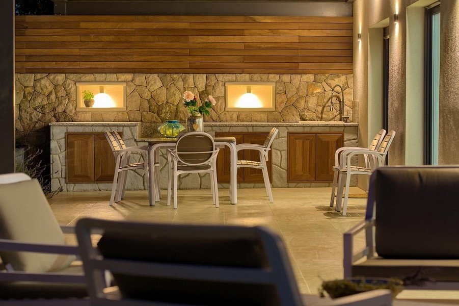 Krytý venkovní jídelní kout s kamenným kuchyňským koutem a dřevěnými skříňkami, stylově osvětlený