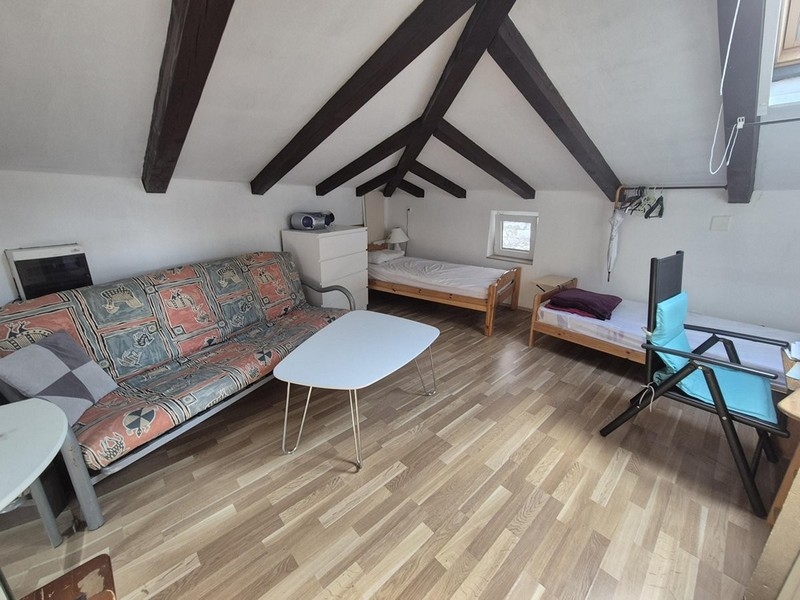 Otevřený obytný prostor v podkroví se dvěma lůžky a dřevěnými trámy na stropě.