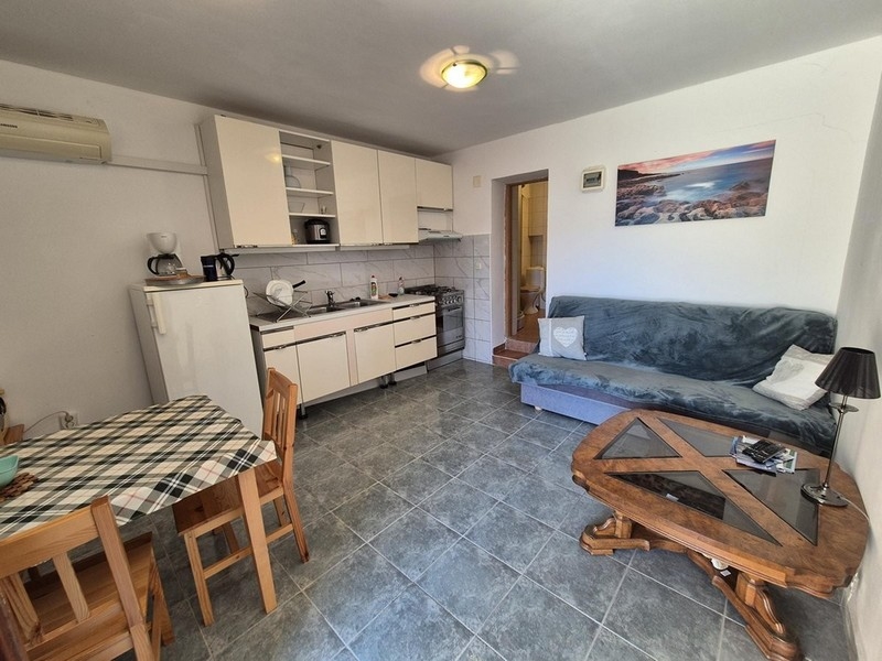 Otevřený obývací pokoj s kuchyní, jídelním stolem a pohovkou, vybavený dlažbou.