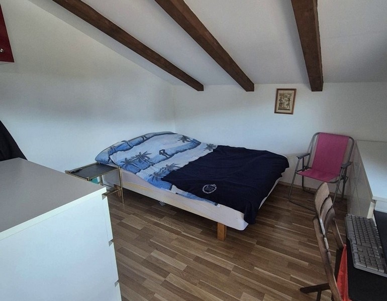 Ložnice v podkroví s dřevěnými trámy a manželskou postelí.