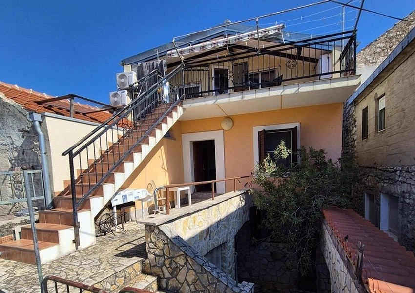 Zadní pohled na středomořský kamenný dům s venkovním schodištěm a terasou.