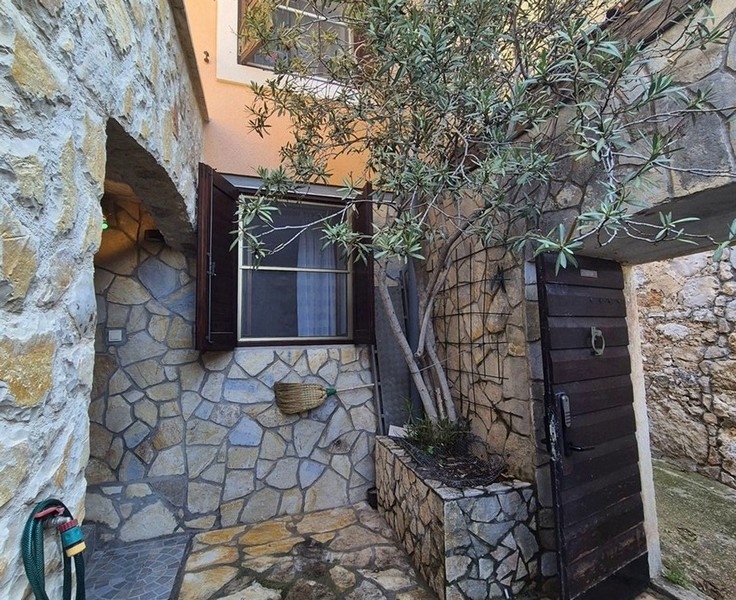 Malé nádvoří s kamennou zdí a olivovníkem, stejně jako vstupní dveře.