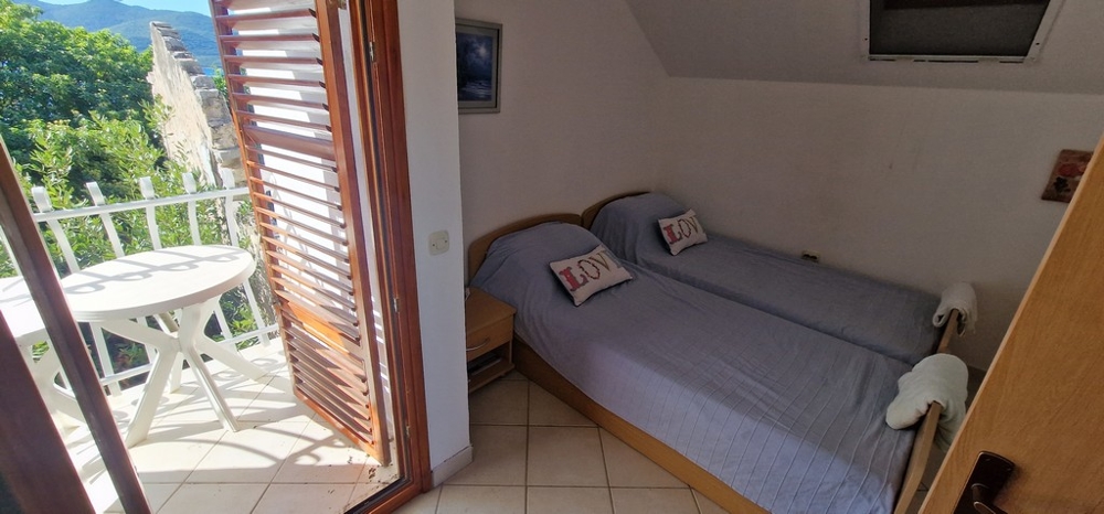 Ložnice se dvěma samostatnými lůžky pokrytými modrými přikrývkami. K dispozici je malý balkon s kulatým stolem a židlemi a výhledem do zeleně.
