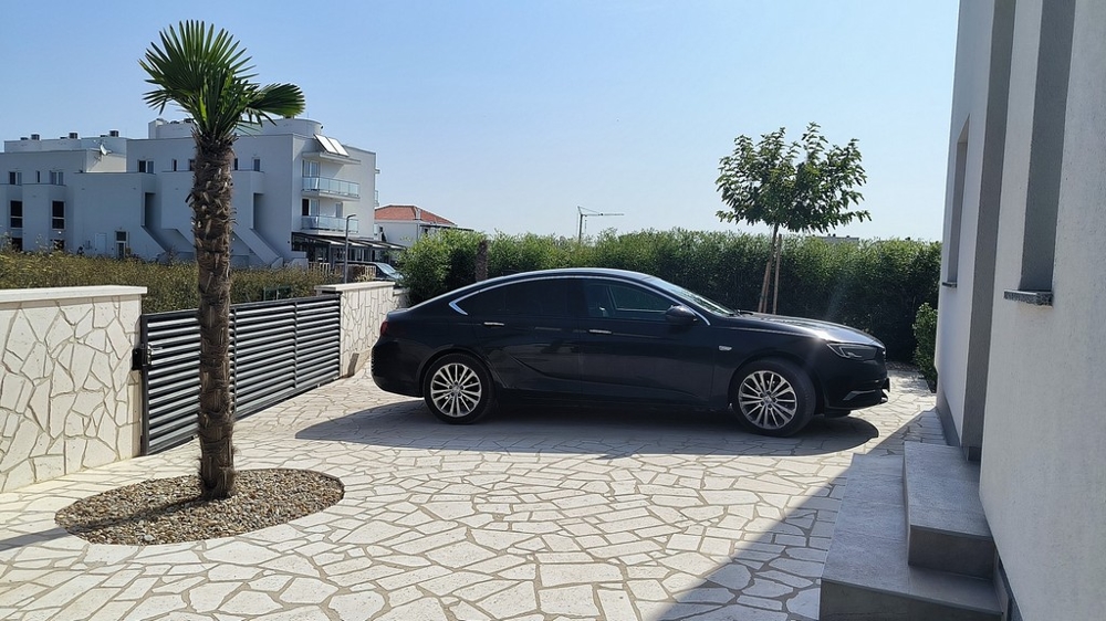 Vchod s autem, palmami a kamennou zdí.