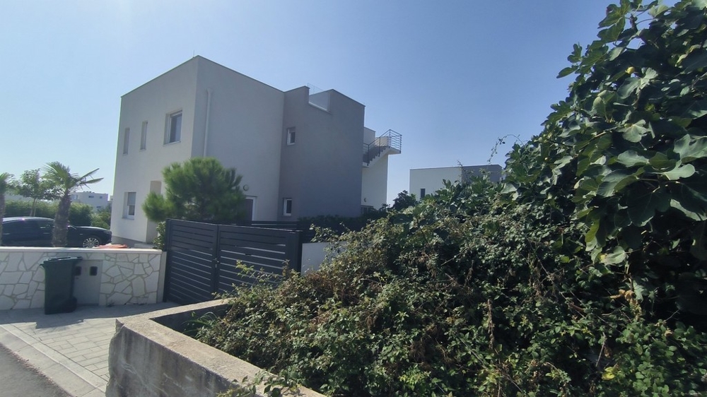 Vnější pohled na moderní dům se zeleným živým plotem a palmami.