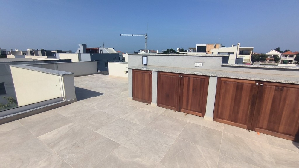 Prostorná střešní terasa s vestavěným dřevěným nábytkem.