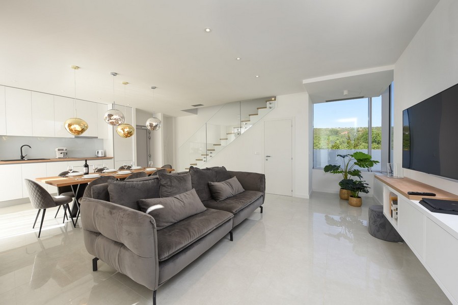 Otevřený obývací pokoj s moderním nábytkem, šedou pohovkou a výhledem do přírody.