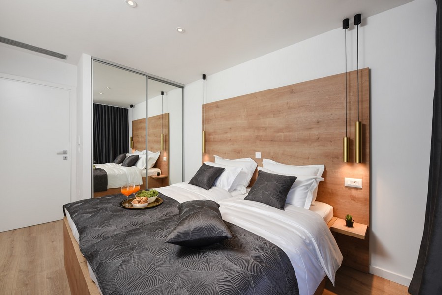 Moderně zařízená ložnice s dřevěnými prvky a šatní skříní se zrcadlovými posuvnými dveřmi.