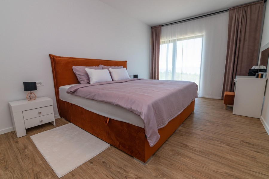 Ložnice s oranžovou postelí a velkými okny