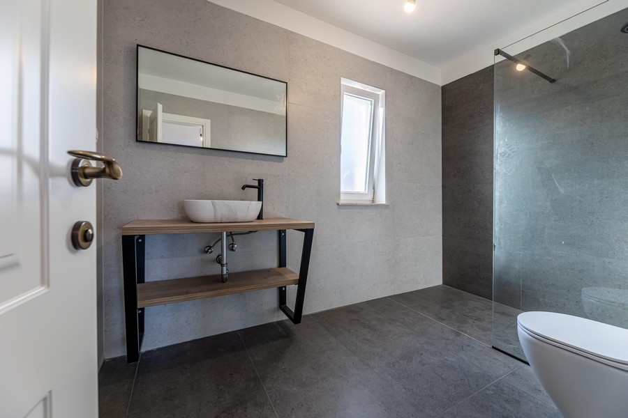 Moderní koupelna se sprchovým koutem a tmavými obklady domu H3481, který se prodává na ostrově Krk.