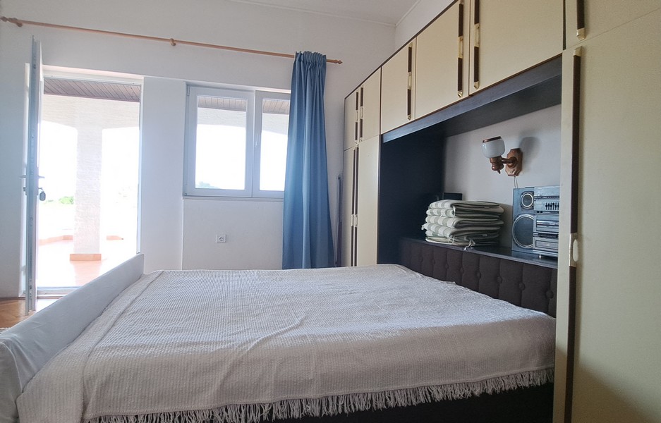 Ložnice s postelí a vestavěným úložným prostorem, výhled na venkovní terasu.