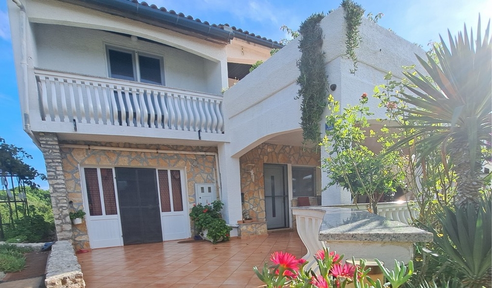 Čelní pohled na dům s balkonem a zahradou.