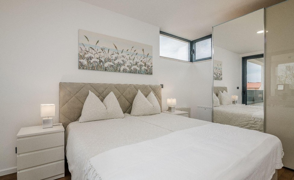 Světlá ložnice s manželskou postelí a zrcadlovou skříňkou