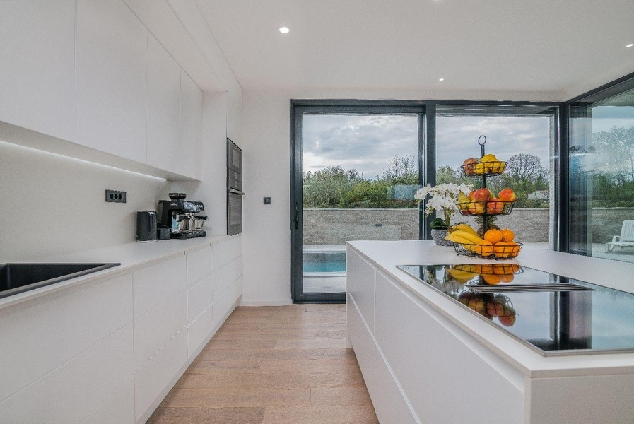 Moderní bílá kuchyně s výhledem na ostrov a bazén