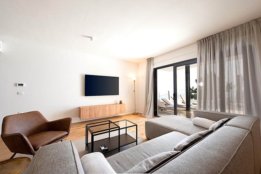 Obývací pokoj s šedou pohovkou, TV a vstupem na terasu