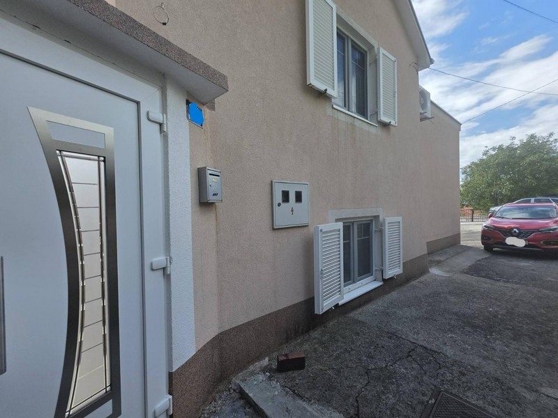 Fasáda domu se vstupními dveřmi, žaluziemi a parkovacím stáním