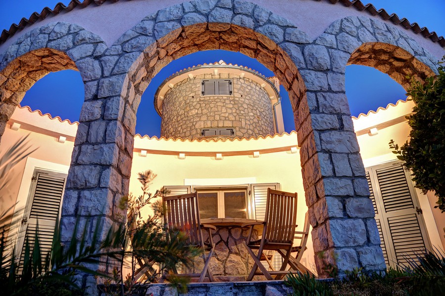 Kamenné arkády a kulatá věž s terasou osvětlenou v noci