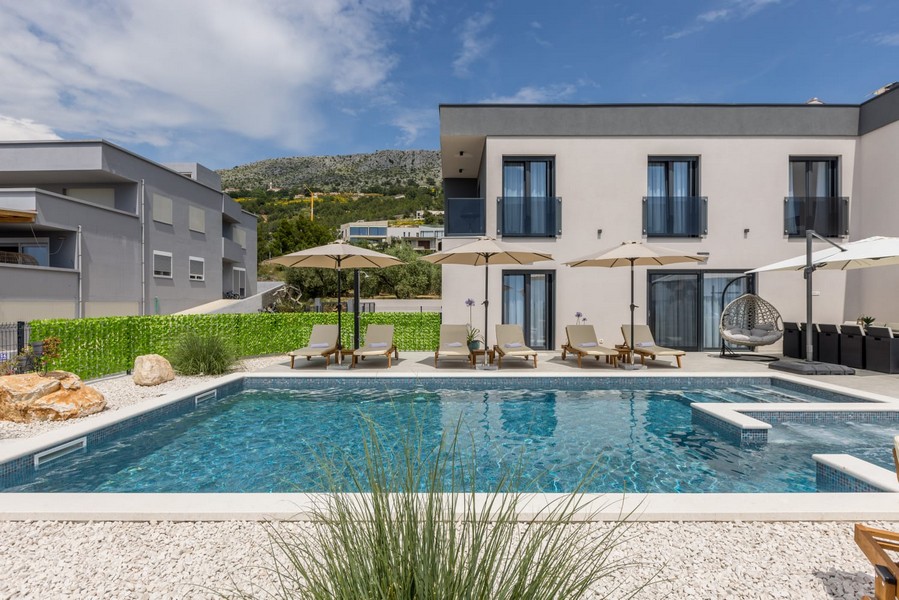 Výhled na bazén s lehátky a moderní vila