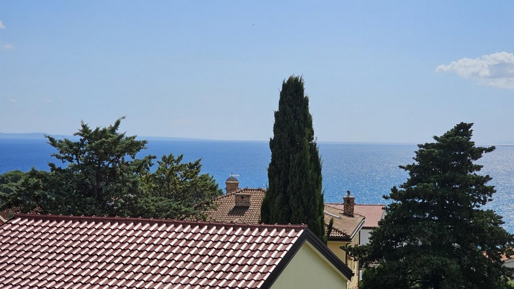 Výhled na moře z balkonu přes střechy a stromy