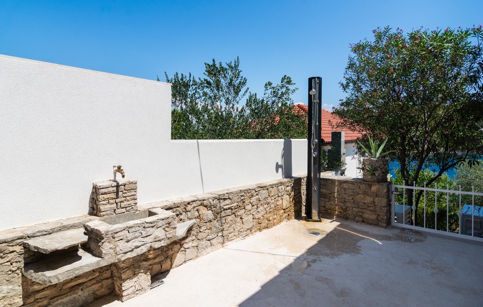 Venkovní prostor s kamennou lavicí, umyvadlem a venkovní sprchou