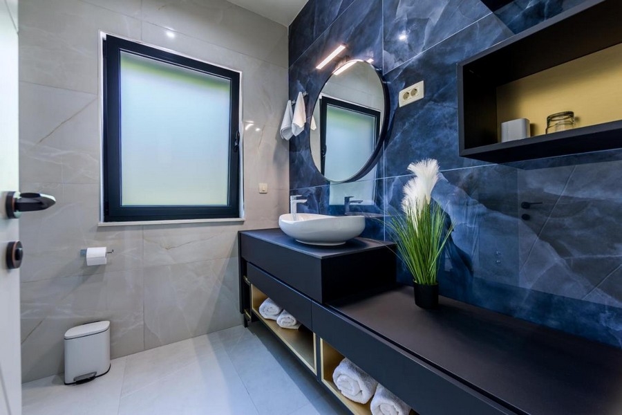 Koupelna s modrou mramorovou stěnou a kulatým zrcadlem