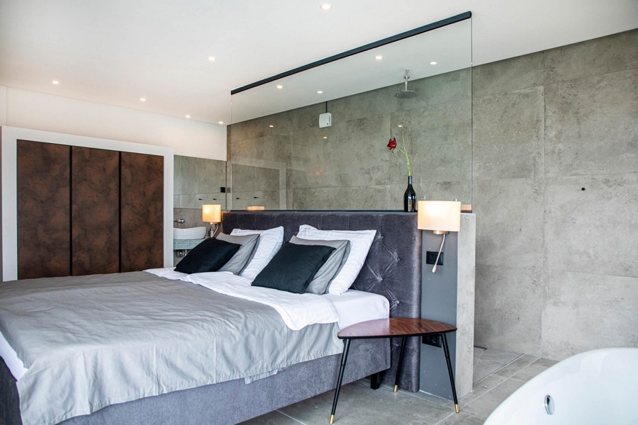 Šedá ložnice s prosklenou stěnou.