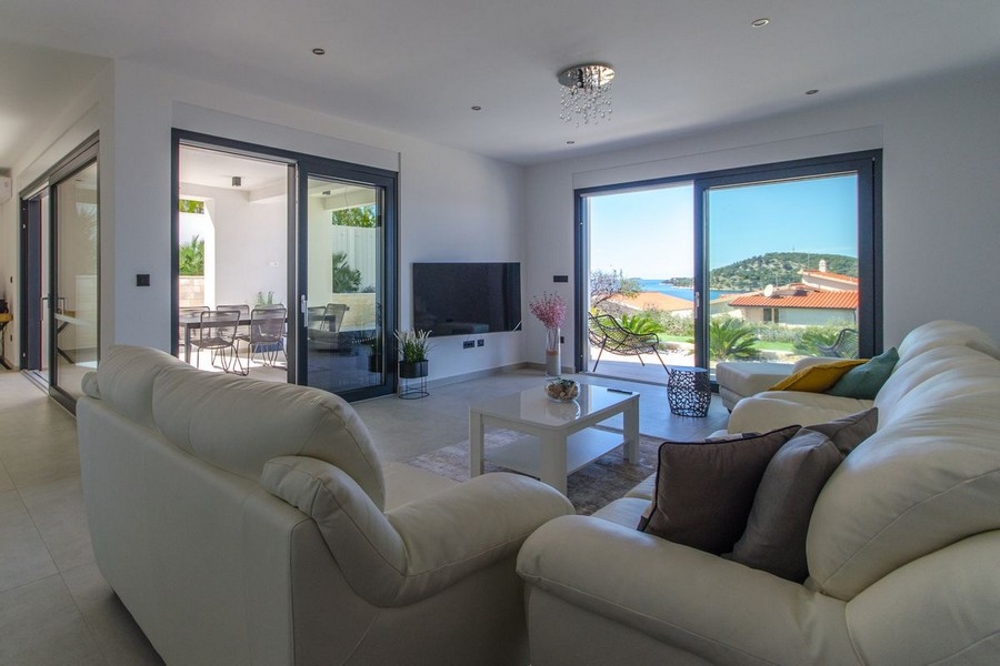 Světlý obývací pokoj s velkým proskleným průčelím a výhledem na moře