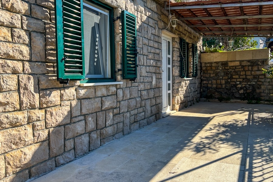 Kamenná terasa se vstupem do domu a zelenými okenicemi