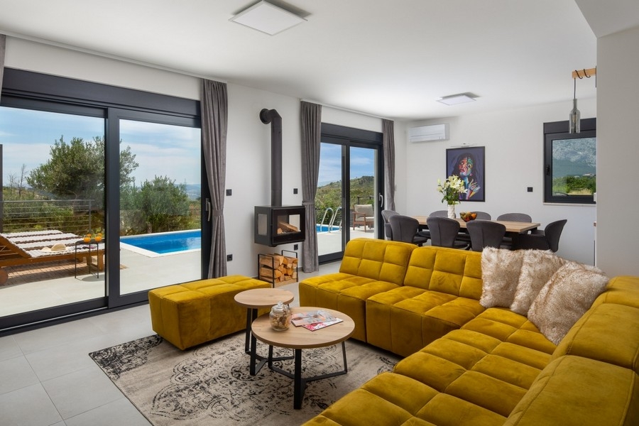 Obývací pokoj s pohovkou, krbem a vstupem na terasu u bazénu